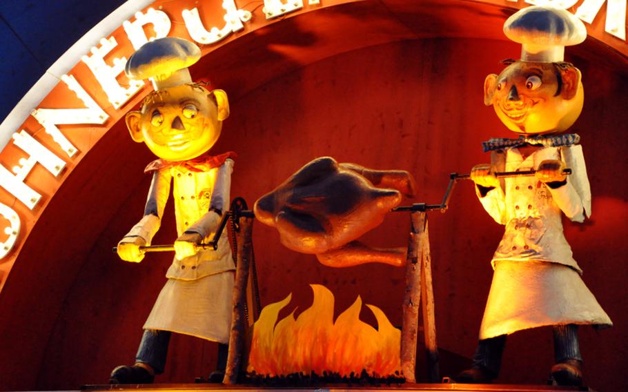 An animated statue roasts a chicken over an open flame rotisserie-style, designating where to find food at Oktoberfest in Munich on the first  Saturday of the fest. Other food vendors have similar displays telling patrons what kind of food they are serving.