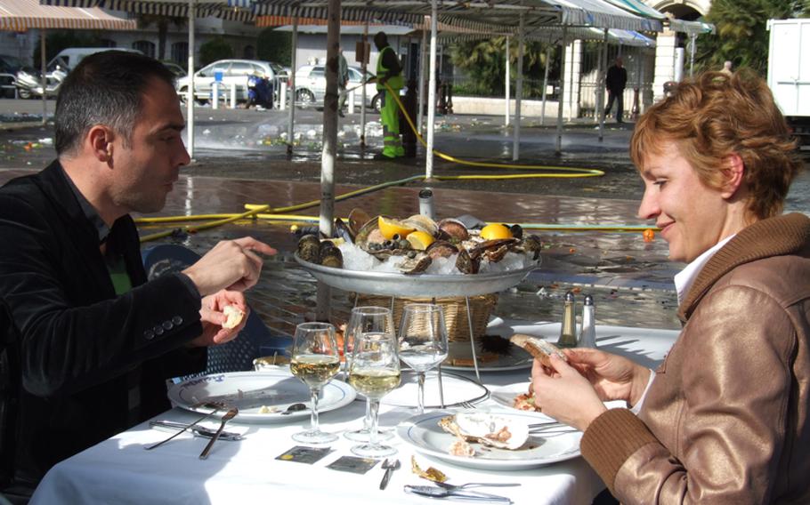A couple enjoys seafood at an outdoor restaurant in Nice's marketplace as workmen clean the streets of the just-closed market in the background.
