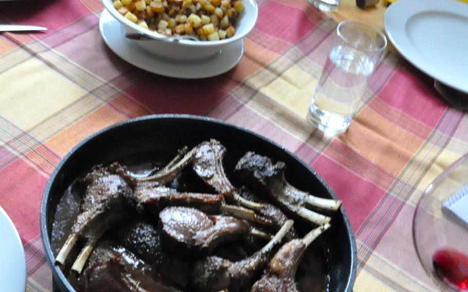 A pan full of tender lamb chops, sauteed, with a plum sauce on the side, is served with two family-style bowls of vegetables, home fried potatoes and  sliced steamed carrots in a dill sauce.