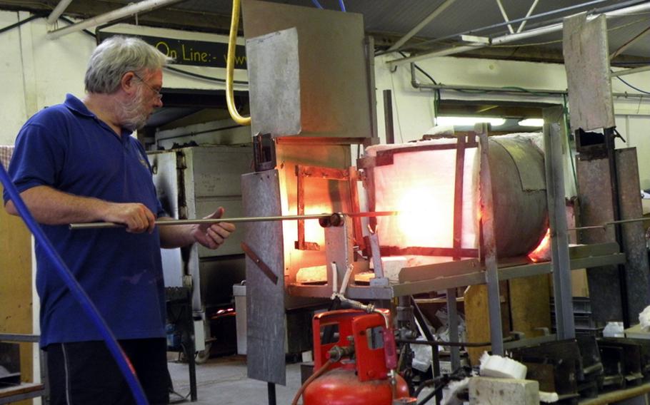 Glassmaker John Wainwright places a rod with molten glass attached into a furnace.