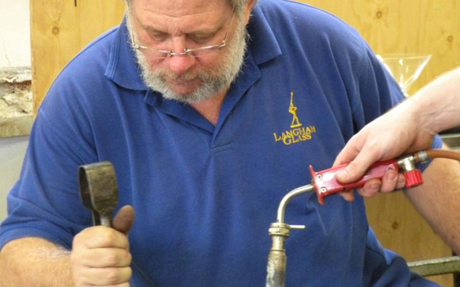 Glassmaker John Wainwright uses a pair of clamps to manipulate the stem of a wineglass while his colleague, Ian Richardson, uses a torch to keep adequate heat on the piece.