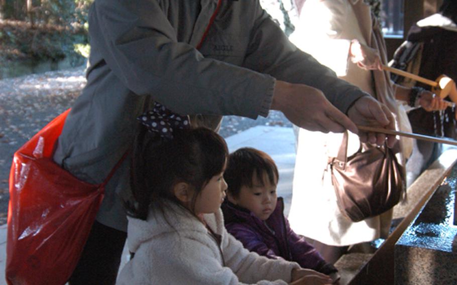 Children put their hands out to have them washed at temizuya, or the water basin, at Meiji Jingu before entering the main shrine. Worshippers are expected to wash their hands and mouths before entering the altar to pray in order to cleanse themselves.