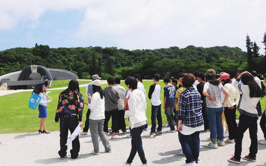 A group of students listens to a tour guide talk about the Hill of Peace. The large structure is meant to represent a cave where many Okinawans hid during the Battle of Okinawa.