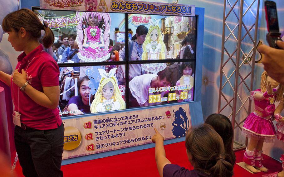 Massive TV screens project live footage of people walking through an exhibit and projected girly, anime-style clothing onto their bodies at the 2011 Tokyo International Toy Show.