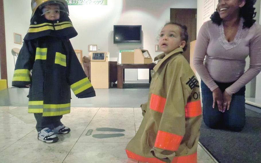 Three-year-old Dallin Wightman, left, and 1-year-old McKenna Wightman play dress-up at the Tokyo Fire Museum as their mother, Leslie, looks on, laughing.