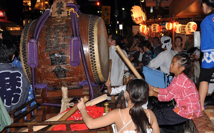 Children beat a drum while everyone prepares to move a shrine to another location.