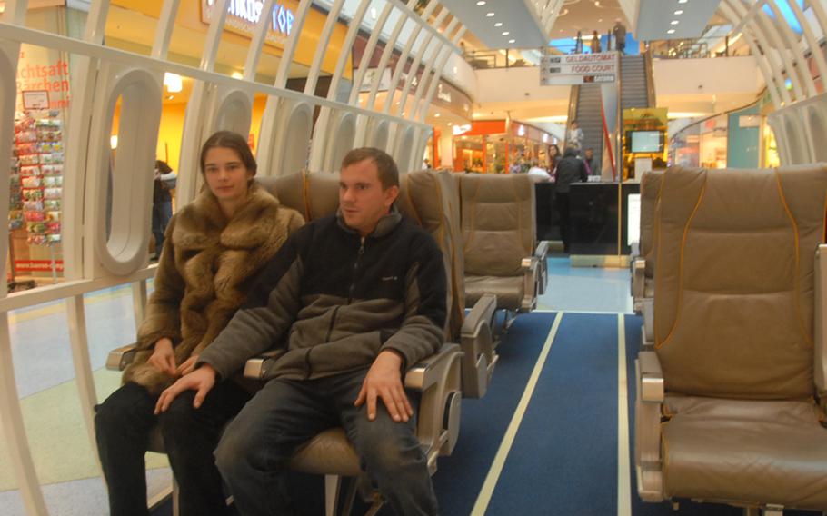 Aviation is the theme of the Loop 5 Shopping Centre near Darmstadt, Germany, and  Frankfurt Airport. One of the ways it illustrates that is by positioning dozens of airline seats throughout the center where shoppers can relax. Taking advantage of one of the rest areas is Jasmine Frost and her husband, Heiko, a local couple.