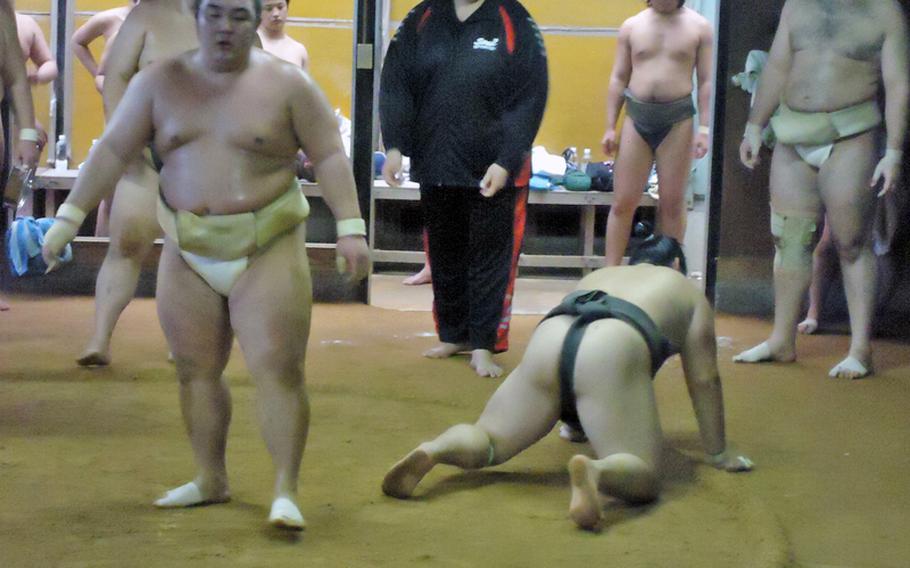 A coach looks on smiling as one wrestler picks himself up out of the dirt and another looks to his next opponent during training at the Sadogatake sumo wrestler stable in Fukuoka recently.