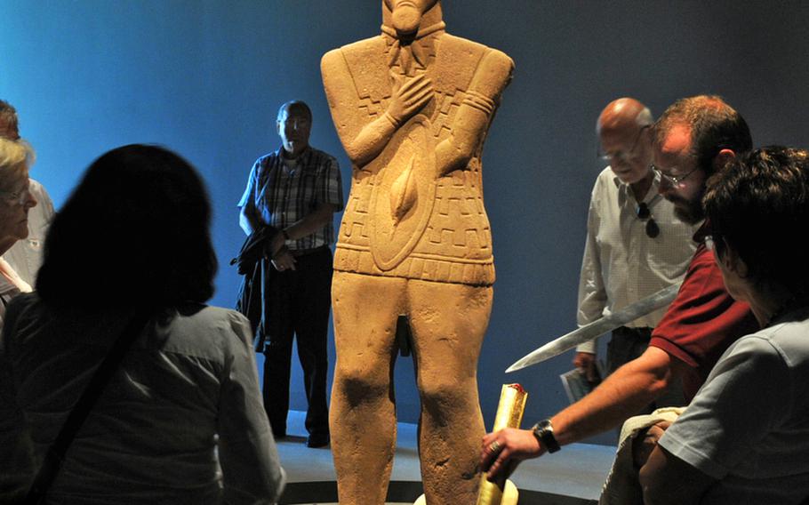 A statue of a Celtic ruler watches over a demonstration by Stephan Medschinski, a guide at the Keltenwelten am Glauberg museum. Medschinski was showing a replica of the original sword found inside the ruler's grave.