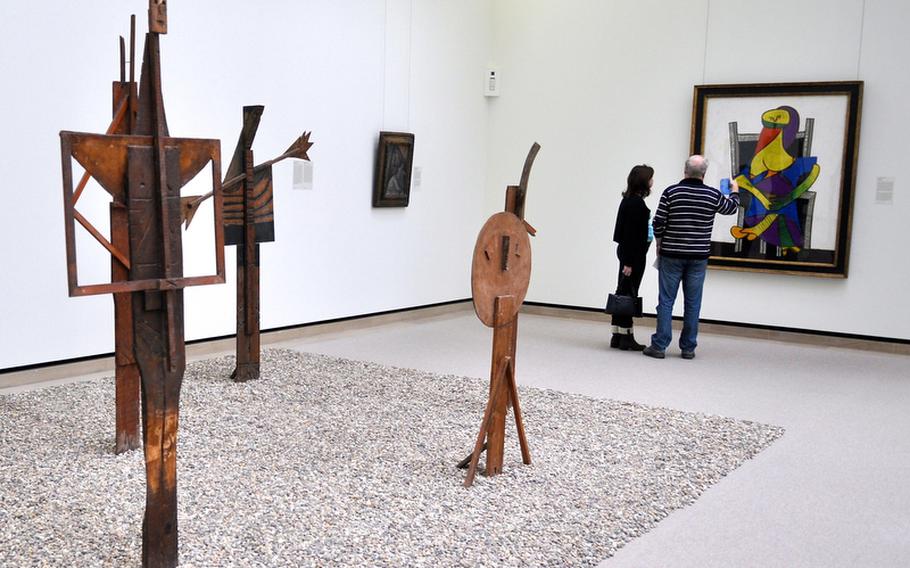 A couple discusses a painting by modernist artist Pablo Picasso in a room dedicated to Picasso's works at the Staatsgalerie in Stuttgart, Germany. In the foreground are some sculptures by the famed artist.