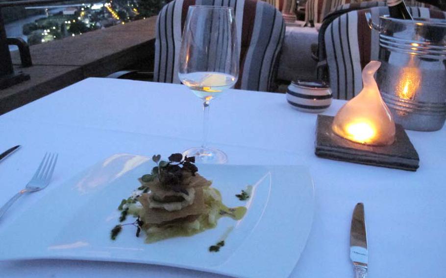 An appetizer of scallops with lemongrass puree and fennel-orange vegetables rests near a glass of wine and a candle before being devoured at the Hirschhorn Castle restaurant.