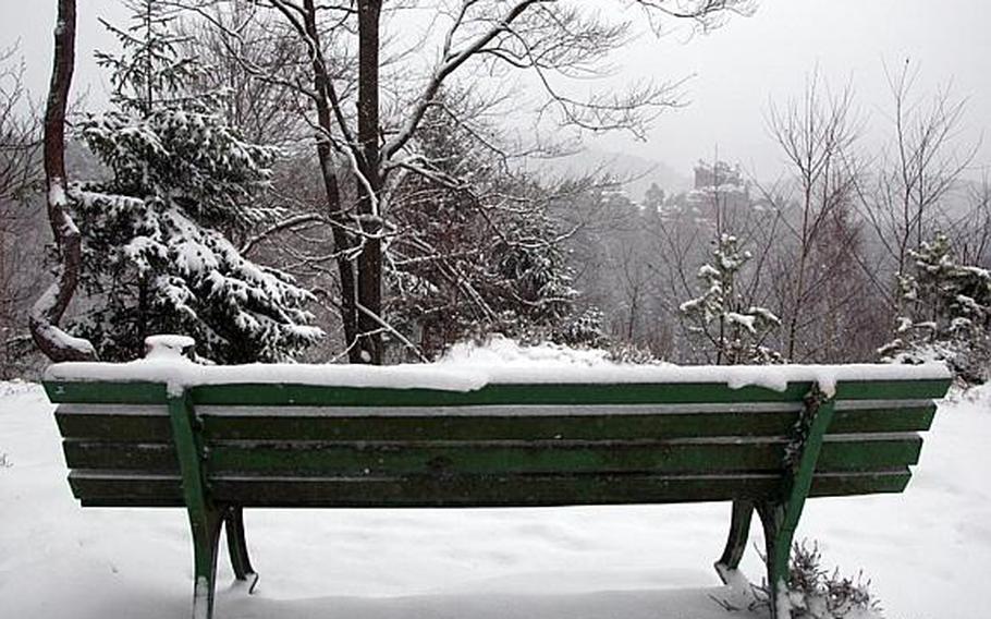 A snowy bench on the Dahner Felsenpfad's Lammerfelsen overlook has a permanent view of another sandstone spire rising out of the woods on another part of the trail near Dahn, Germany.