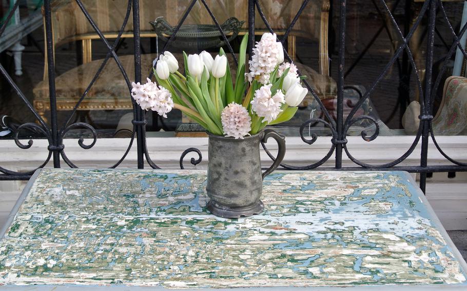 Fresh flowers sit in a vase on a table in front of an antique store.