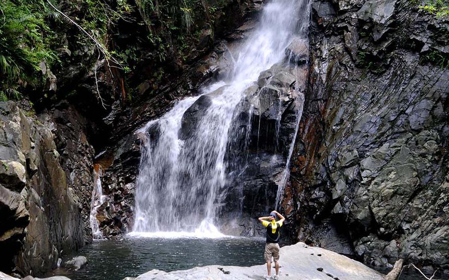 Although off-limits, many tourists can't resist climbing as close as possible to the Hiji waterfall at Hiji Falls National Park, Okinawa, Japan.
