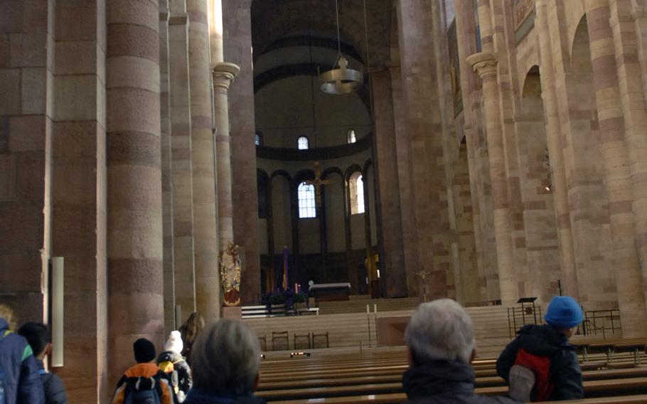 Visitors to the cathedral in Speyer, Germany, sit in pews inside the basilica's central nave, a towering room flanked by sandstone pillars.