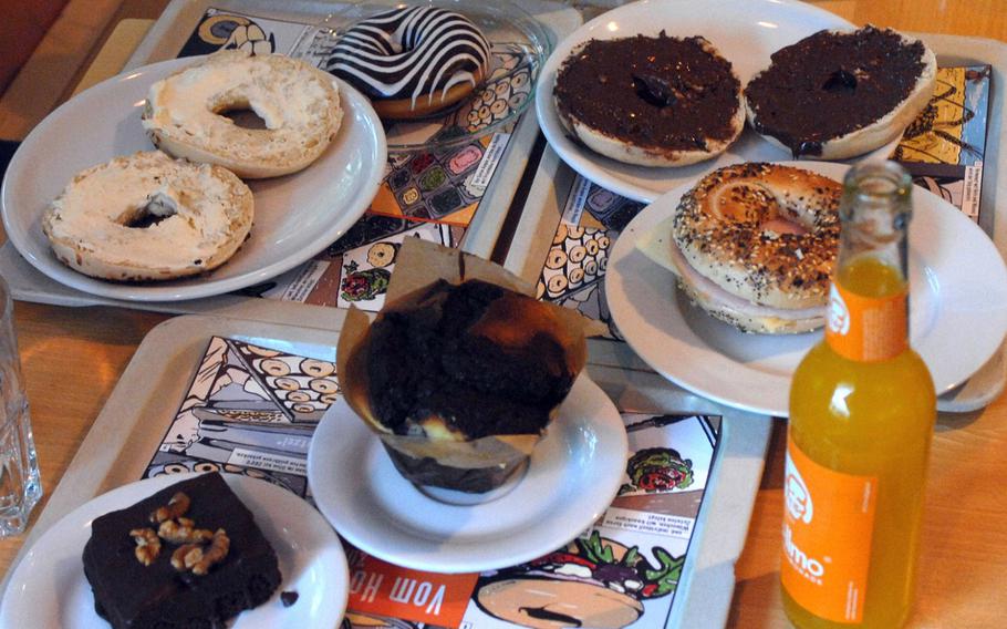 A breakfast spread featuring bagels, muffins, brownies, coffees and bottled fruit juice occupies a table at Bagel Brothers in Frankfurt. A family ordering a variety of things in June pronounced this assortment delicious.