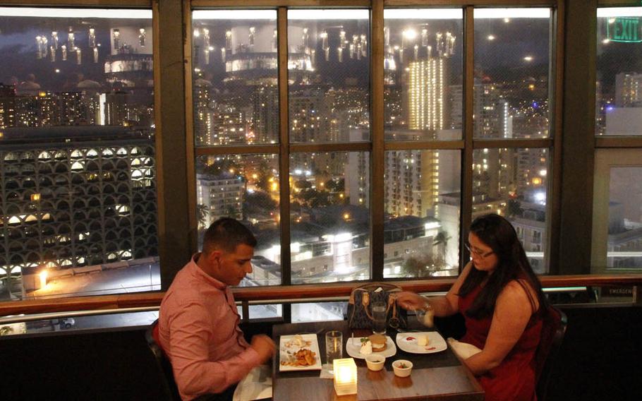 Diners enjoy their meals at Top of Waikiki as the lights of Honolulu flicker outside.