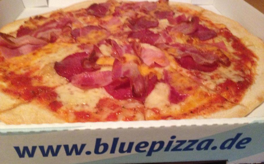 A large London pizza is delivered from Blue Pizza, a new pizza takeout and delivery place in eastern Kaiserslautern, Germany. The London pizza is topped with ham, salami, bacon and cheddar cheese.