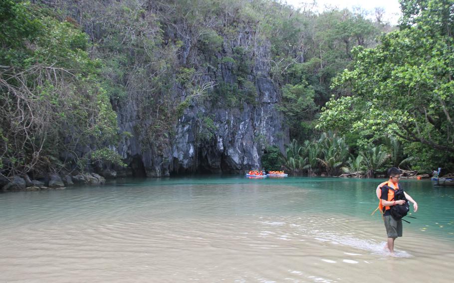 A boat prepares to enter the Puerto Princesa Underground River while another departs. The boats are steered and propelled by a single boatman using a long wooden pole.