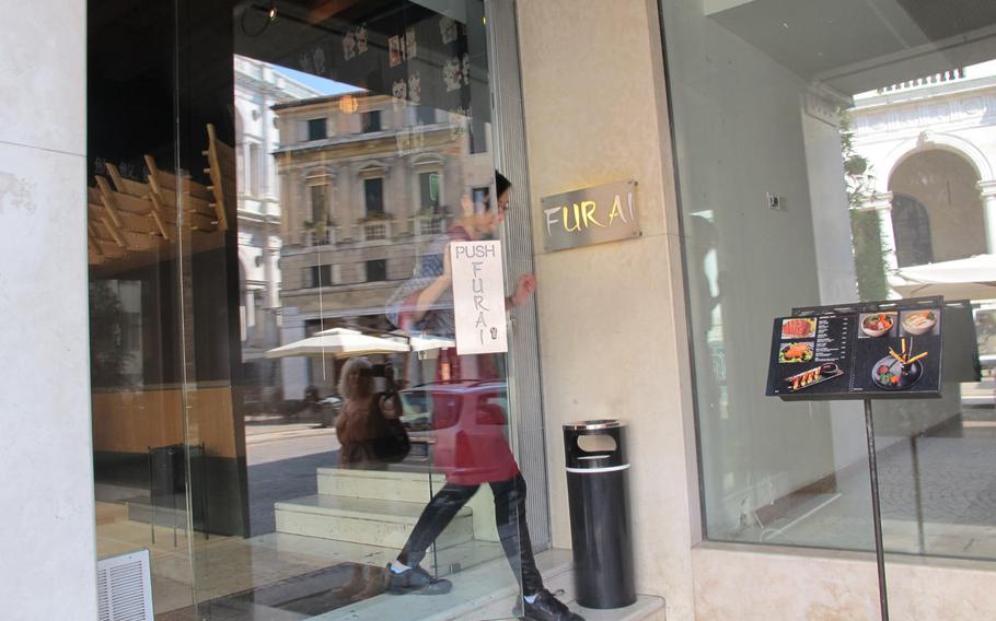 A friendly staffer at the Furai Japanese Restaurant in Vicenza, Italy, on the way to attend to a diner seated in the plaza outside.