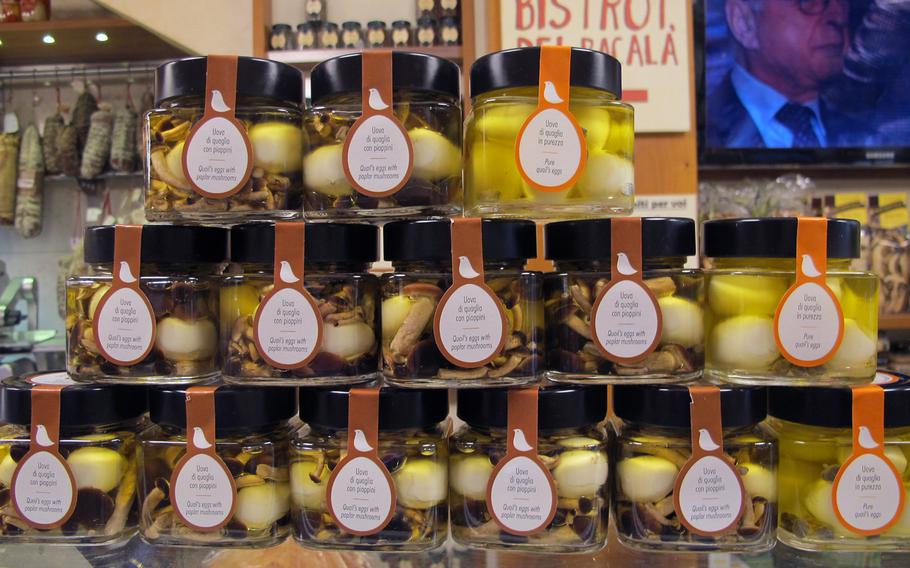 Jarred quail eggs and mushrooms are stacked on the counter at Il Ceppo in Vicenza, Italy. On the screen in the background is patriarch Osvaldo Boscolo, who founded the business 45 years ago. Always elegantly attired, he often works the cash register.