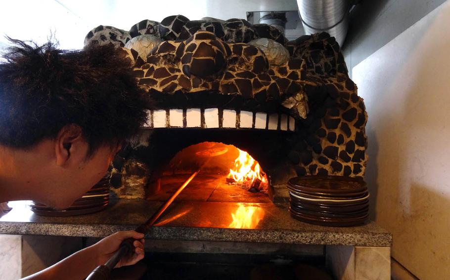 Masanao Souma, owner and chef of Pottery and Cafe Gunjo, carefully places a pizza in a stone oven shaped like the head of a shisa statue. Just like making pottery, fire plays a crucial role in the process.