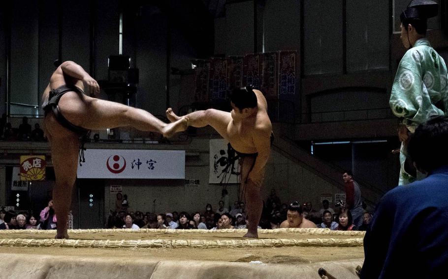 Sumo wrestlers enter the ring, face each other and lift their legs high in the air before stomping them down to scare away demons.
