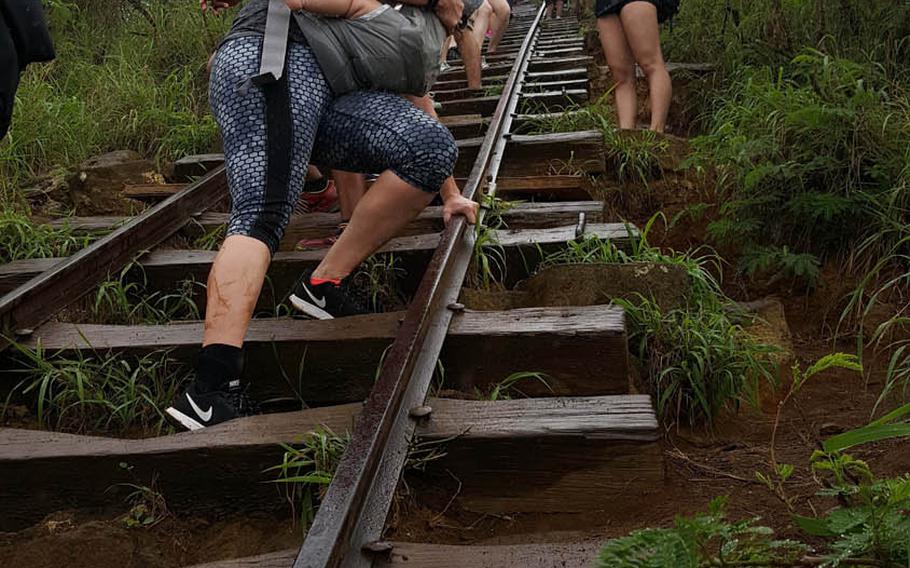 A climber gingerly descends the steps of Koko Crater Trail with an infant strapped to her chest. Rain has made the rail ties slippery.