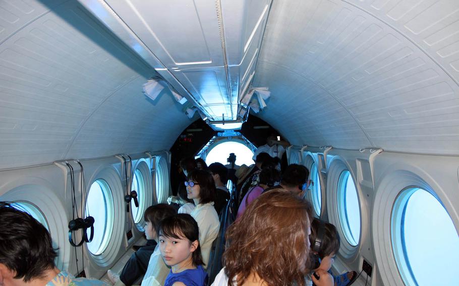 Passengers look through large portholes on the side of an Atlantis submarine during a recent tour. In the background, the sub's pilot sits at the controls.