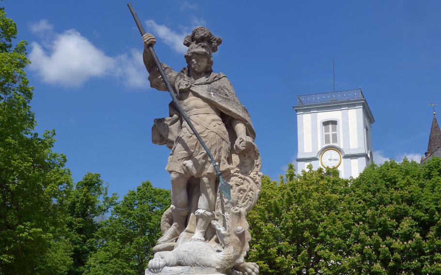 The St. George's fountain on the Friedberg Castle grounds, with the steeple of the 18th century Castle Church in the background. The St. George statue is a copy, the original is in the nearby Wetterau Museum.