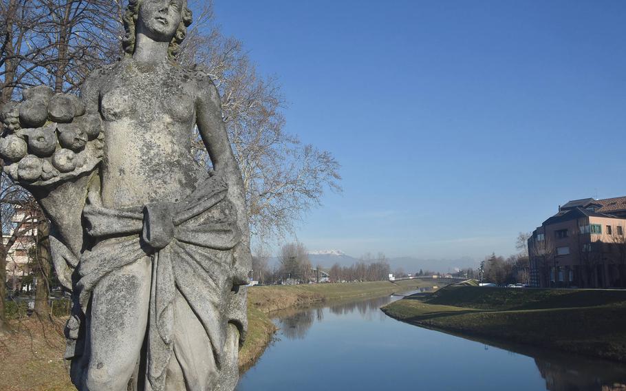 A statue on one of the two bridges to span the Monticano River in Oderzo, Italy, gazes toward the downtown area and away from the countryside and snow-topped mountains that loom in the horizon.