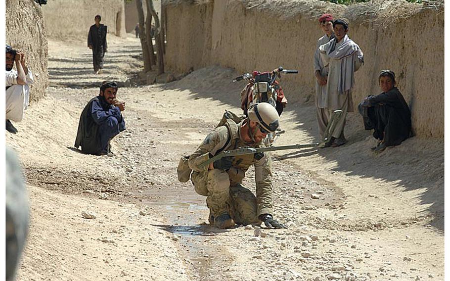 A Navy explosive ordnance disposal technician searches for an IED while locals watch in Zabul Province, Afghanistan in Sept. 2010. Military leaders say the number of bomb disposal experts should remain steady even as the military begins its pull back from Afghanistan.