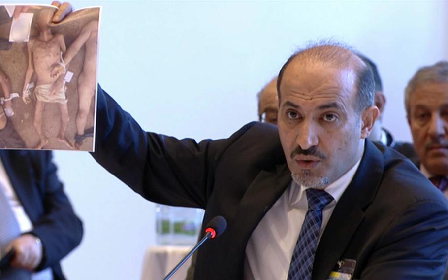 In an image taken from UNTV, Ahmad Assi al-Jarba, the head of Syria's Western-backed Syrian National Coalition, holds up an image of alleged torture victims during the Syrian peace talks in Montreux, Switzerland, Wednesday Jan. 22, 2014.