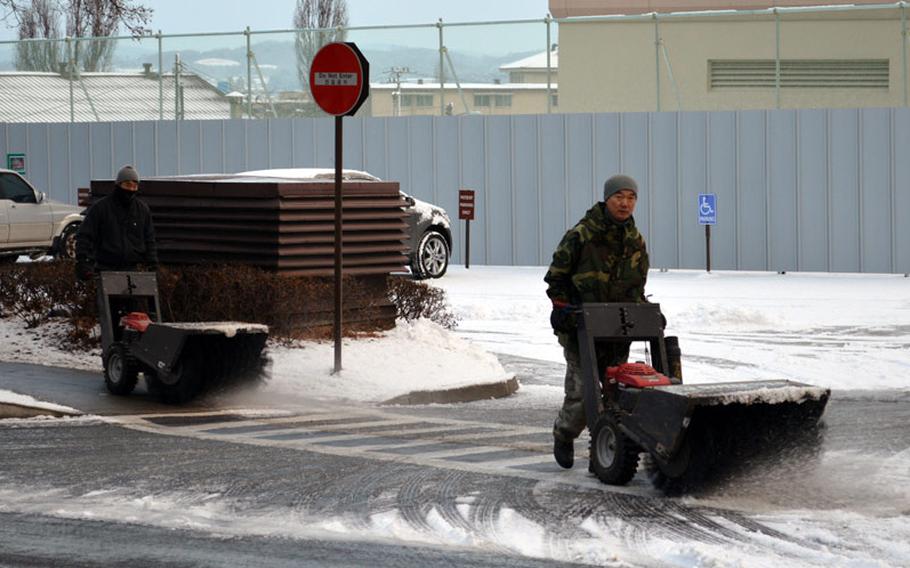 A pair of South Korean workers clears a snow-covered sidewalk at Osan Air Base, South Korea, on Dec. 11, 2013.
