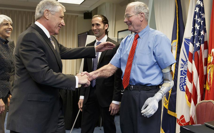 Defense Secretary Chuck Hagel, left, reaches out to embrace Fred Downs, a wounded Vietnam War veteran he served with and who has been fitted with a prototype prosthetic arm and hand developed by DARPA, the Defense Advanced Research Projects Agency, Tuesday, April 22, 2014, at the Pentagon. At center is Justin C. Sanchez, center, a program manager with DARPA. Hagel was getting a look at the latest high-tech projects being developed for wounded warriors.