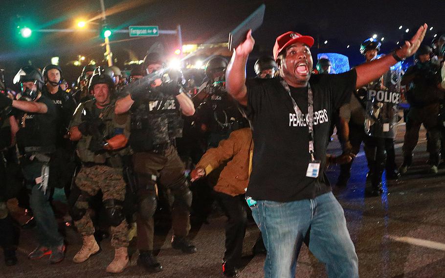 A citizen peacekeeper tries to keep protesters back as police advance Monday, Aug. 18, 2014, in Ferguson, Mo.