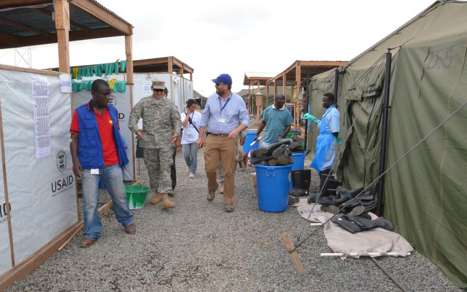 Andrew Lind, right, project coordinator for the International Organization for Migration, takes soldiers of the 36th Engineer Brigade, out of Fort Hood, Texas, on a tour around the Ebola treatment unit after its grand opening, Buchanan, Liberia, Dec. 22, 2014, as part of Operation United Assistance. 