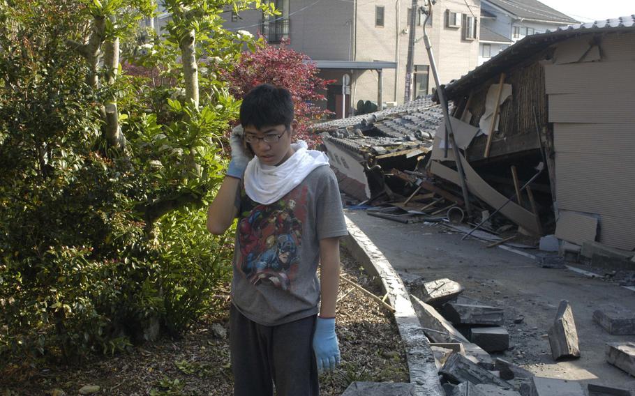 Takumi Hamasaki, 14, talks on the phone near earthquake-damaged homes in Mashiki, a small town near the city of Kumamoto, Japan, on Tuesday, April 16, 2016. 

