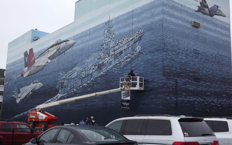 Virginia Beach artist Sam Welty signs a mural he painted in 2013 paying military tribute. The lessee who runs a Howard Johnson in the building sparked controversy when he painted over the mural this week to seal leaks.