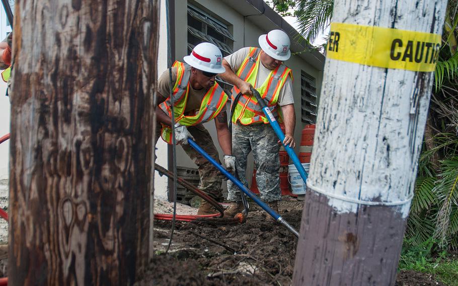 Pfc. Michael Bailey shovels debris as  and Pfc. Dennis Canavan uses a hydraulic tamper at a work site in a neighborhood near San Juan, Puerto Rico, on Nov. 10, 2017.