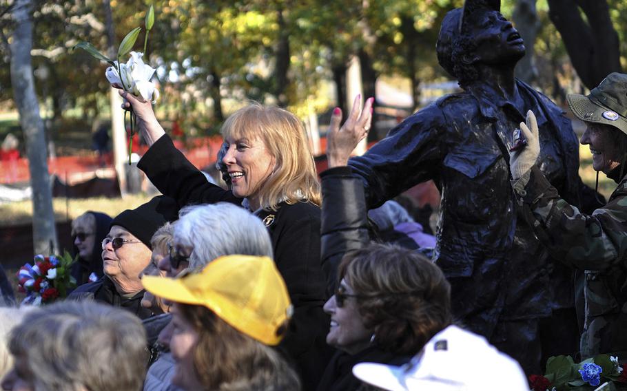 Janis Nark of Aspen, Colo., holds up flowers during a group photo at the Vietnam Women's Memorial on Sunday, Nov. 11, 2018. About 60 Vietnam nurses traveled from across the country to attend the event, which marked 25 years since the memorial was established on the National Mall.