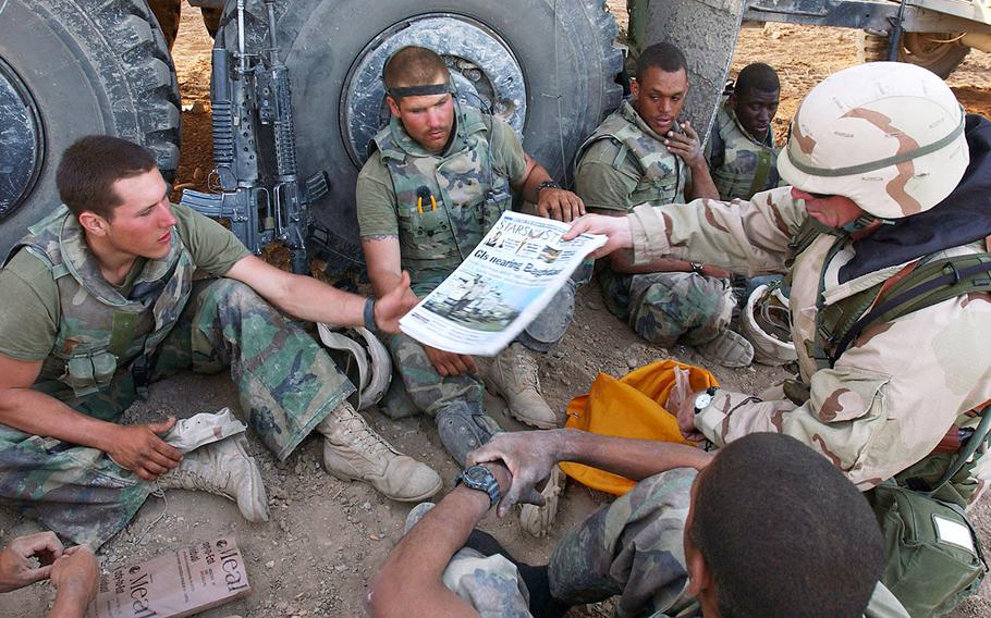 In a 2003 photo, Command Sgt. Maj. John Sparks delivers copies of Stars and Stripes to U.S. Marines from Weapons Platoon, 3-2 India Company. The Marines were part of Task Force Tarawa, deployed in support of Operation Iraqi Freedom.