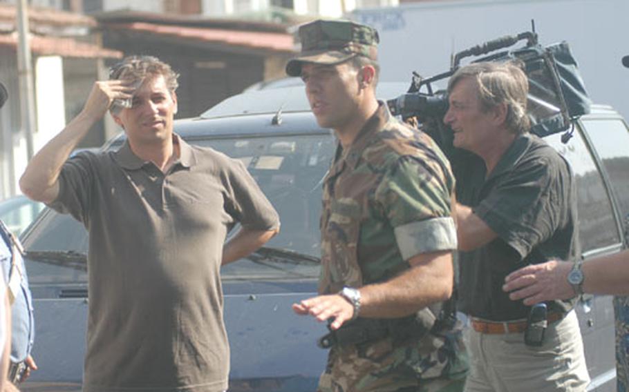Petty Officer 3rd Class Jeff Schoff, center, a master-at-arms, acts out a traffic accident scene with "victim" Fiorello DePalma, left, a translator for Naples Security, during filming Thursday for a recruiting video. The cameraman is Mauro Caiano.
