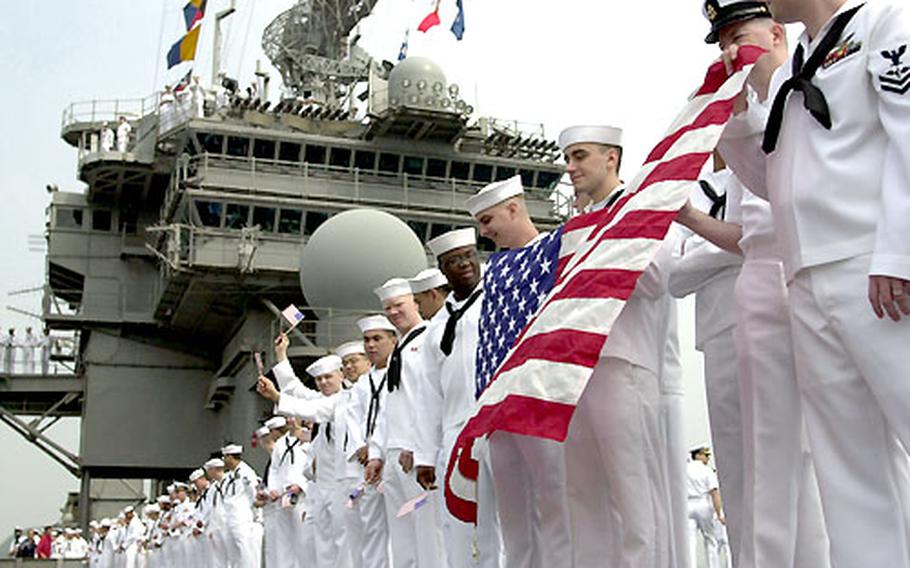USS Kitty Hawk sailors man the rails, flags in hand, as the ship pulls into Yokosuka May 6 following its Persian Gulf deployment.