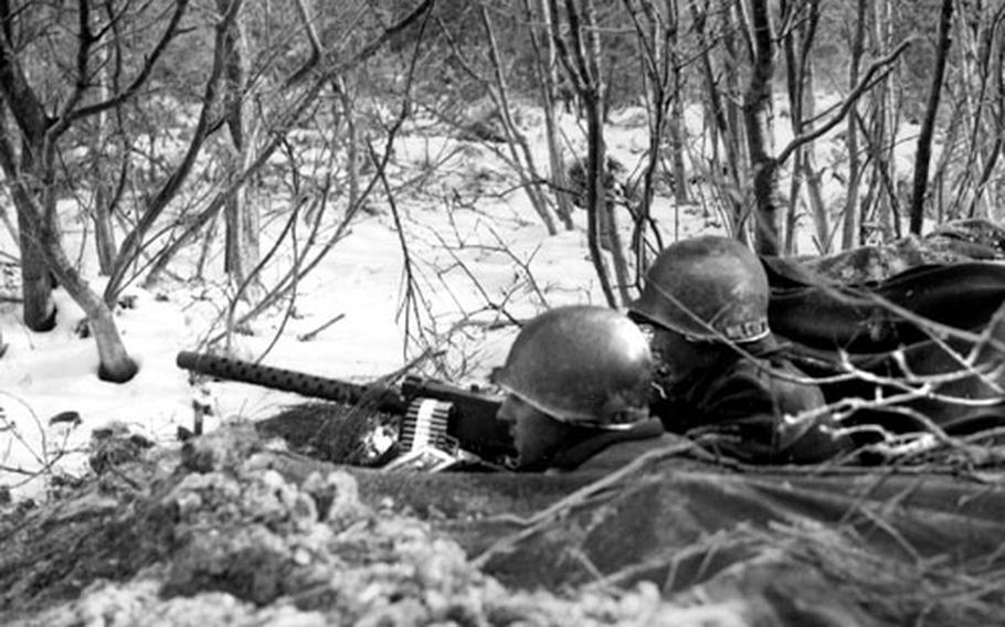 Two U.S. soldiers, dug into the snow and dirt east of Bastogne, Belgium, man .30-caliber light machine guns as they keep an eye out for German troops.