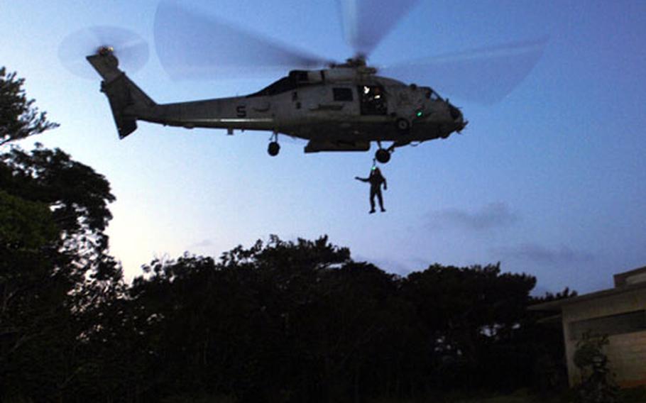 A Navy air crew member is extracted by a Navy HH-60G helicopter from the aircraft carrier USS Kitty Hawk during a non-combatant evacuation operation at Combat Town training area, Okinawa, Japan, during Joint Air and Sea Exercise 2005 here. Air Force pararescue airmen and sailors rescued “U.S. Embassy personnel” trapped in a building.