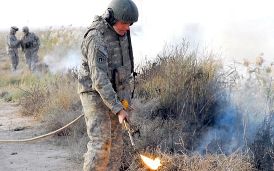 Sgt. Jeremy Bell, of the 3rd Platoon of the 15th Engineer Company, uses an acetylene torch to set fire to brush along a roadway in Iraq during a recent route sanitation mission near Muqdadiya in north central Iraq. The missions are intended to remove debris that can be used to hide gunment or explosives along roadways.