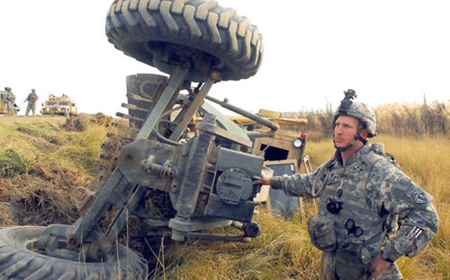 Spc. David Flowers stands beside an upturned road grader moments after he tumbled down an embankment inside the piece of heavy equipment during a route sanitation mission near Muqdadiya.