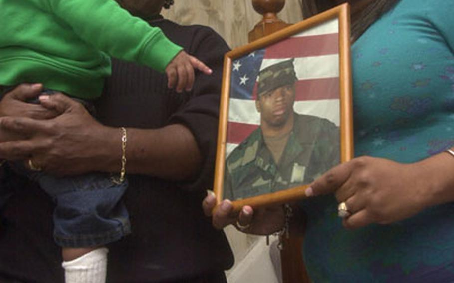 Stephanie Cockrell embraces her grandson Juwan Johnson Jr. while Johnson Jr.’s mother Kenika Johnson holds a photo of her late husband.