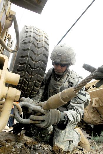 Spc. Krzysztof Socha secures a towing cable to the rear bumper of the stuck Humvee.